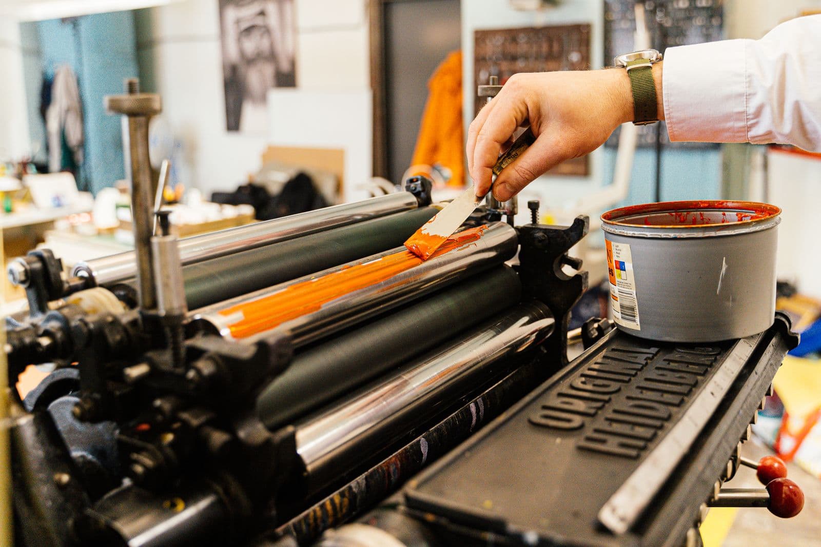 Hand inking a printing press roller with orange ink